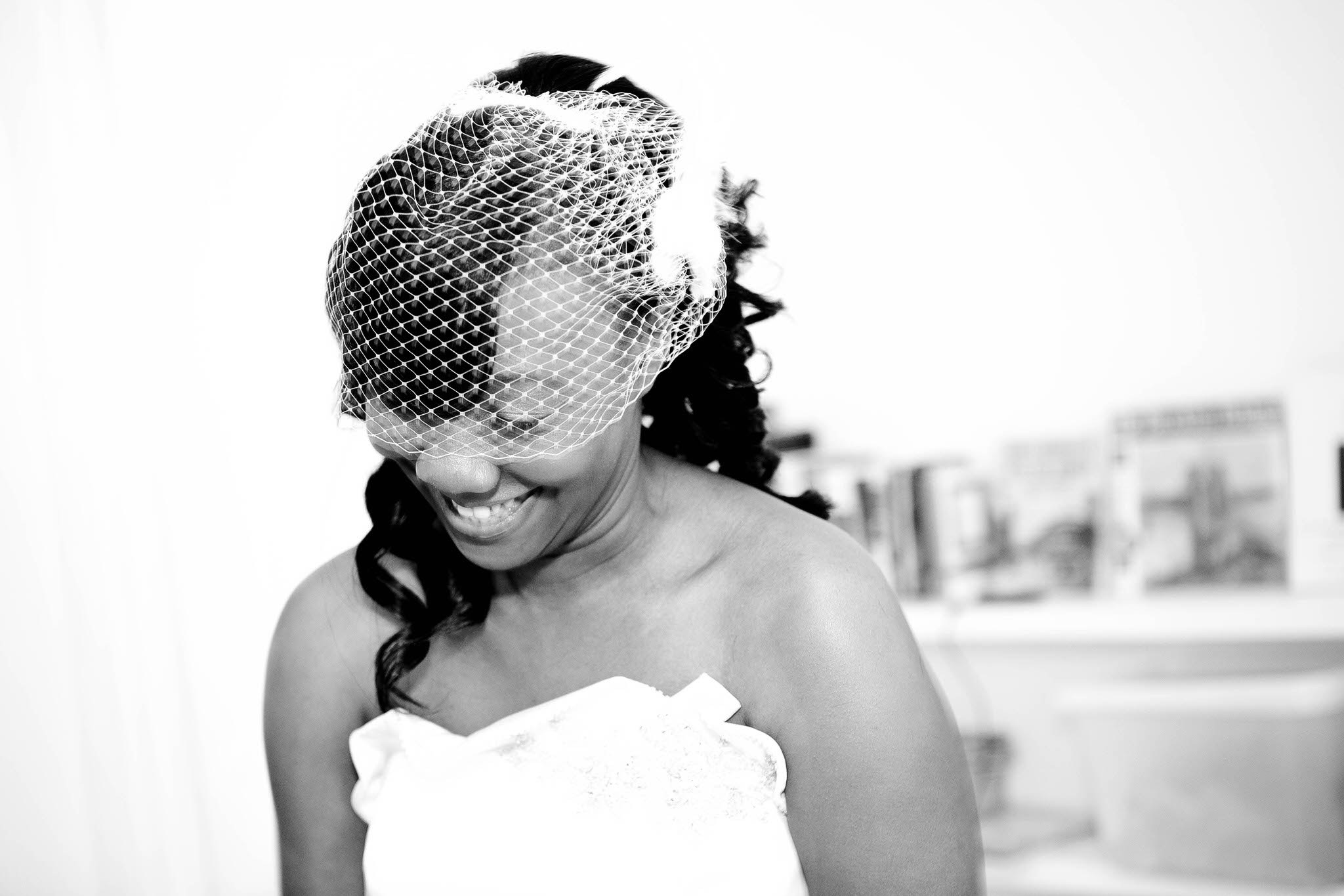 A bride smiles beneath a birdcage veil, in black and white