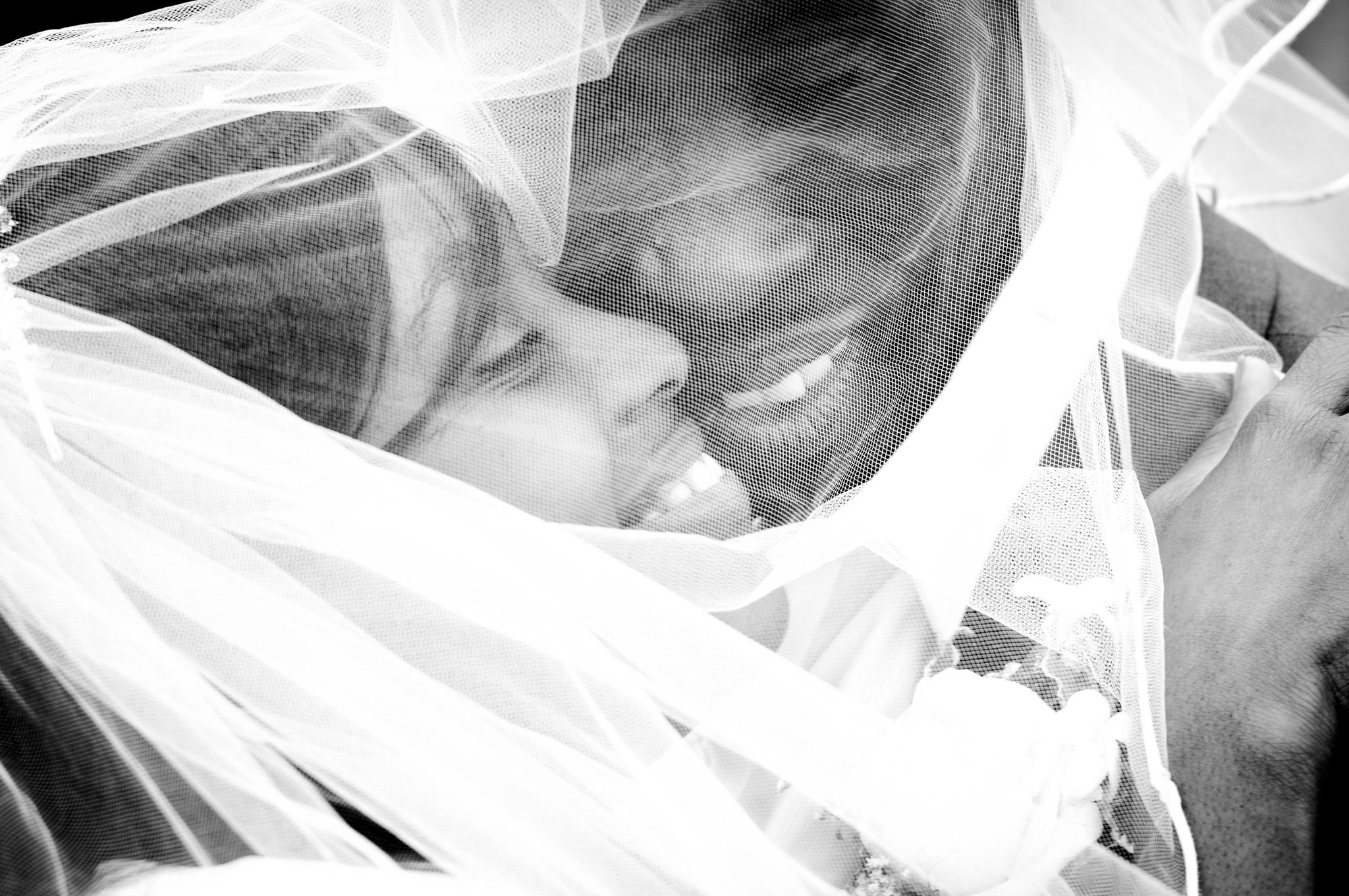 A couple close together under a sheer veil, in black and white